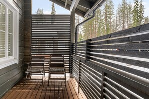 A wooden deck with two chairs and a table, surrounded by a metal fence with horizontal slats.
