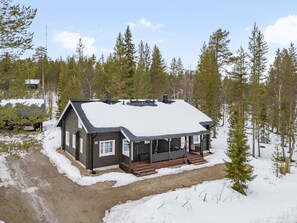 Eine Hütte mit Veranda, umgeben von Schnee und Bäumen.