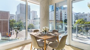 A dining area with a large window, a table set with white flowers, and a view of the cityscape. - Rooftop Retreat + Spa + Pool + Gym | Little Italy District | Ancora by AvantStay (San Diego)