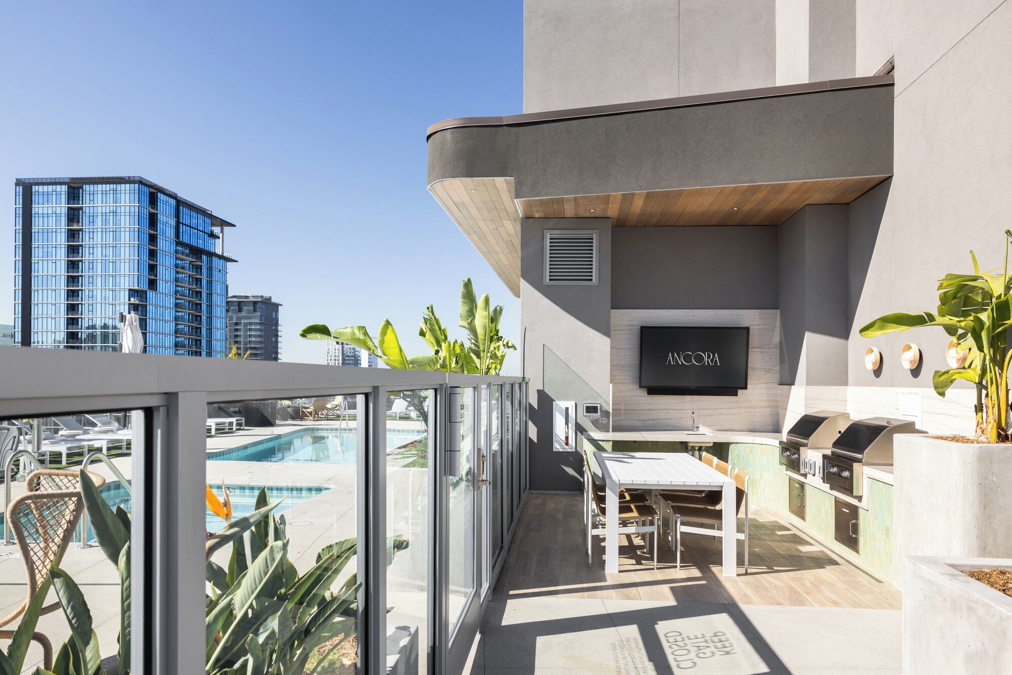 Una terrazza sul tetto con piscina, area salotto all'aperto, barbecue e uno schermo televisivo che mostra 'ANCORA'.