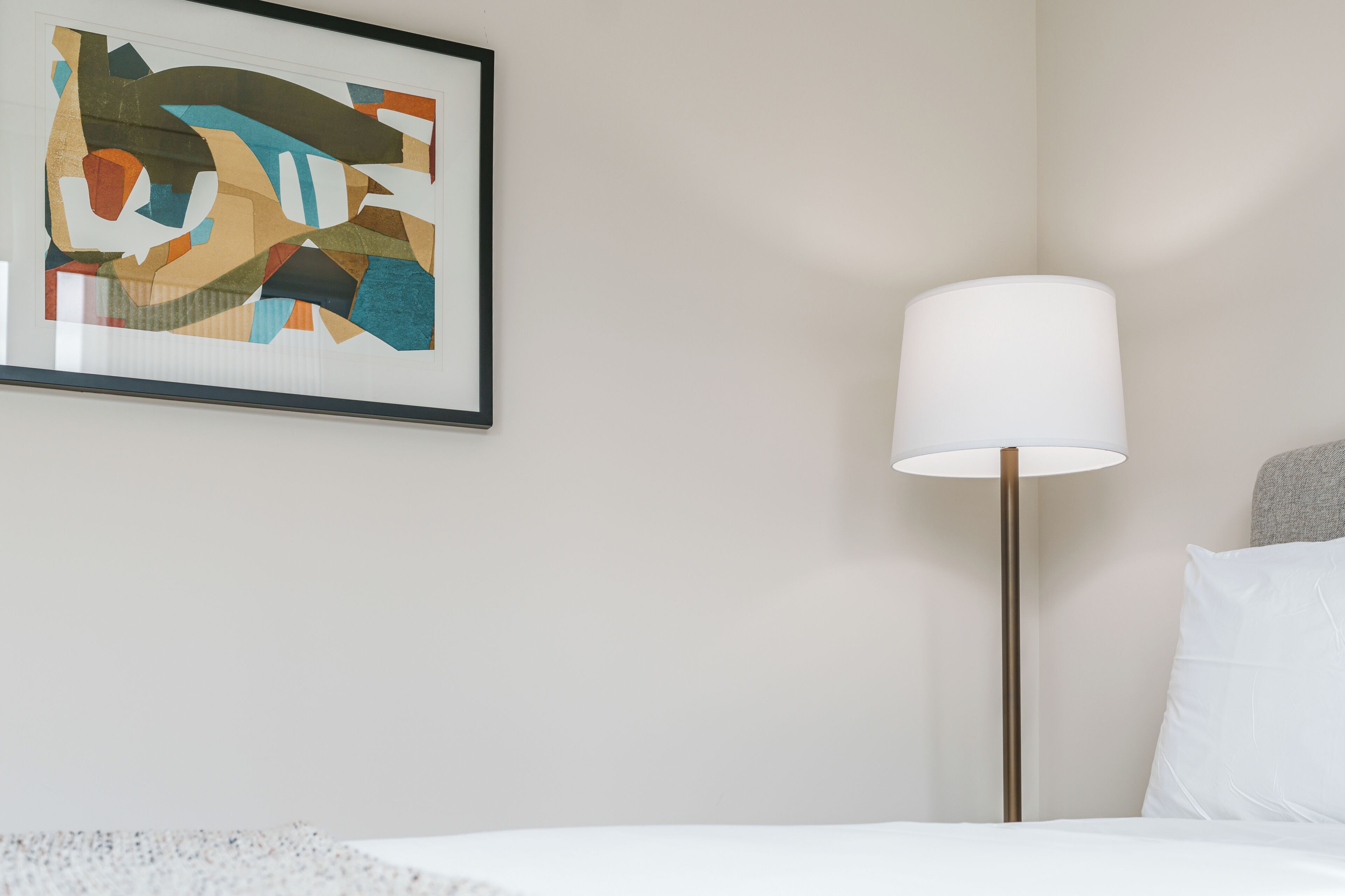 Ett hotellrum med en säng, en golvlampa och en inramad abstrakt målning på väggen.