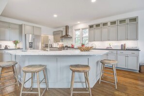 A modern kitchen with a large island, wooden stools, and stainless steel appliances. - Elegant Coastal Retreat w/ Pool, Spa, & Golf Views (Isle of Palms)