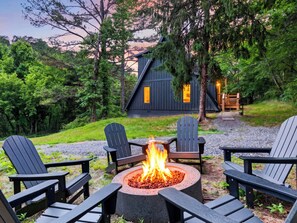 A cabin with a fire pit surrounded by Adirondack chairs, set in a forested area with a gravel path leading to the cabin. - A-Frame Cabin • Hot Tub + Sauna • Near Pigeon Forge | Fireside on Mortar (Sevierville)