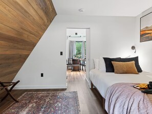 A bedroom with a sloped ceiling, a bed with pillows, a rug, and a view through an open door to a dining area. - A-Frame Cabin • Hot Tub + Sauna • Near Pigeon Forge | Fireside on Mortar (Sevierville)