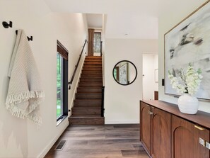 A staircase leading to a second floor, a round mirror on the wall, and a wooden cabinet with a vase of flowers. - A-Frame Cabin • Hot Tub + Sauna • Near Pigeon Forge | Fireside on Mortar (Sevierville)