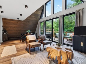 A modern interior with a dining area, seating, and a large window overlooking greenery. - A-Frame Cabin • Hot Tub + Sauna • Near Pigeon Forge | Fireside on Mortar (Sevierville)