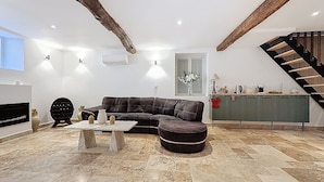 A modern living room with a sectional sofa, a fireplace, a stone-tiled floor, and a staircase.