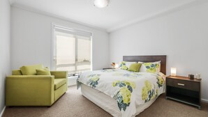 A modern bedroom with a large bed, a green armchair, and a nightstand with a lamp. - Oceanic Stay in central Cowes (Cowes)