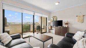 A modern living room with a sofa, a coffee table, a TV, and a balcony with a view. - Oceanic Stay in central Cowes (Cowes)