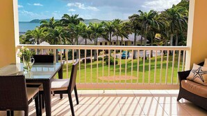 Un balcon avec vue sur une plage et des palmiers, aménagé avec des fauteuils en osier et une table en verre.