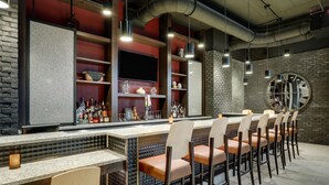 Una zona de bar con una barra larga, varias estanterías llenas de botellas y un gran reloj de pared.
