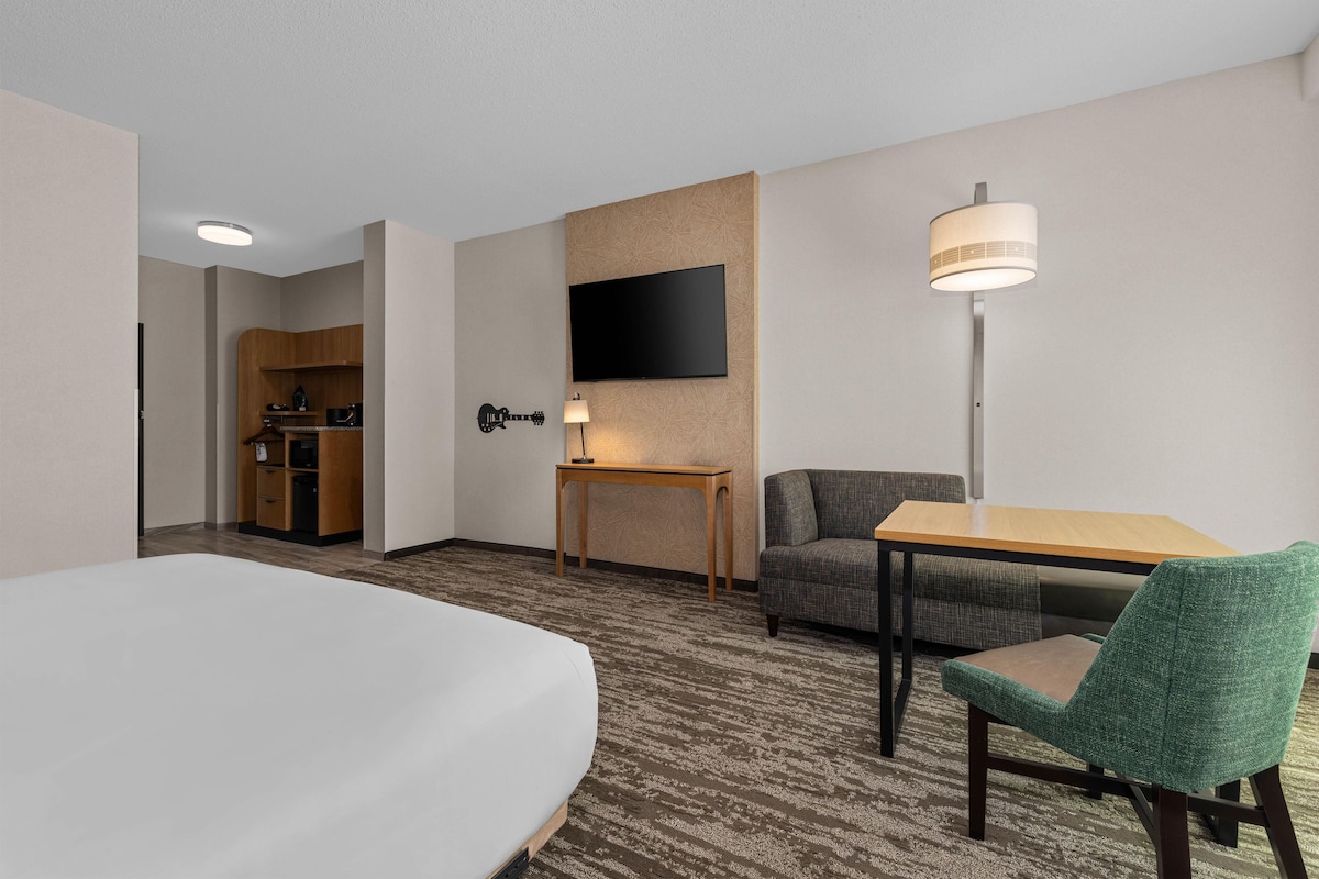 Quarto de hotel com cama, escrivaninha, cadeira, televisão e abajur.