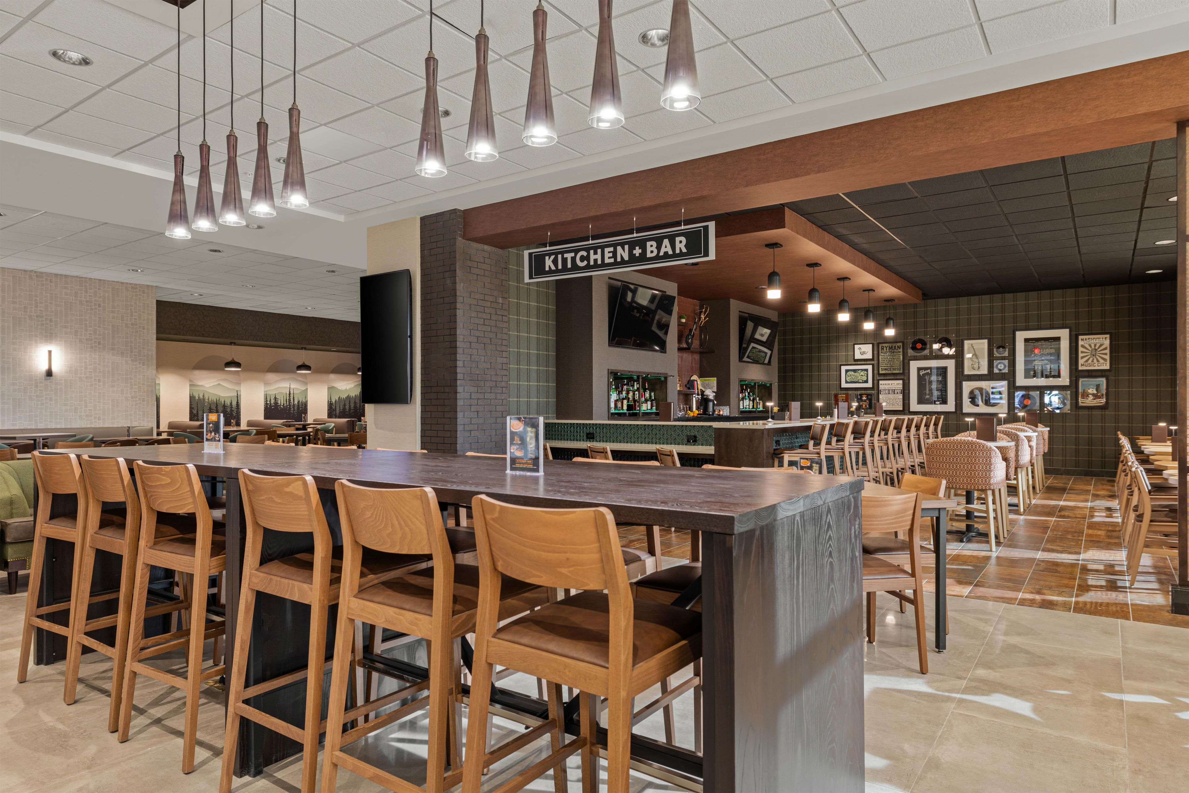 A modern restaurant with a bar area, wooden chairs, and a tiled floor.