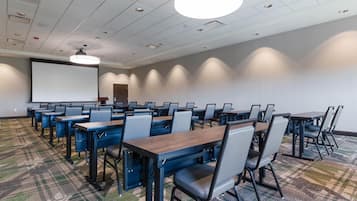 A conference room with multiple tables and chairs, a projector screen, and a carpeted floor.