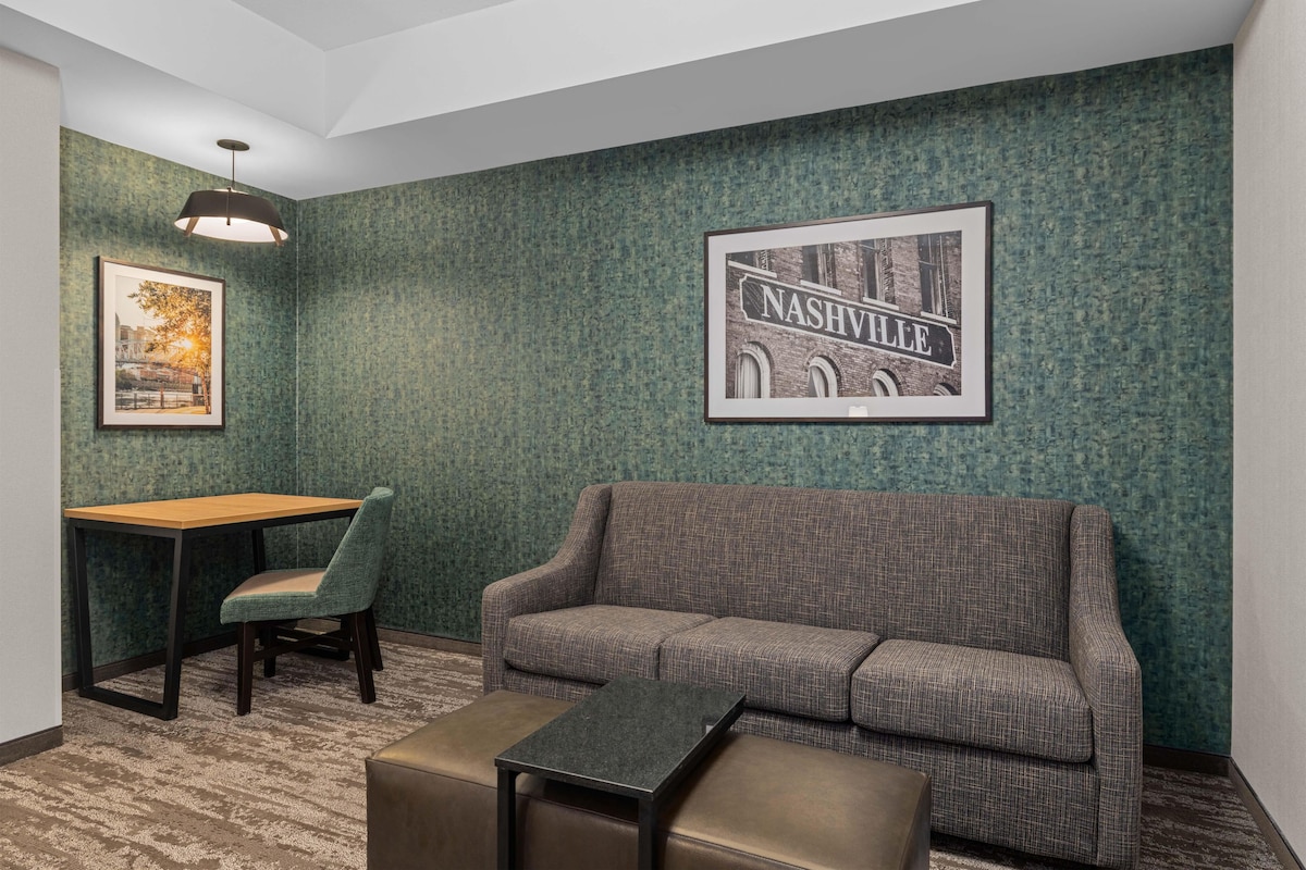Quarto com parede verde texturizada, um quadro de Nashville, um sofá, uma mesinha, uma cadeira e um abajur.