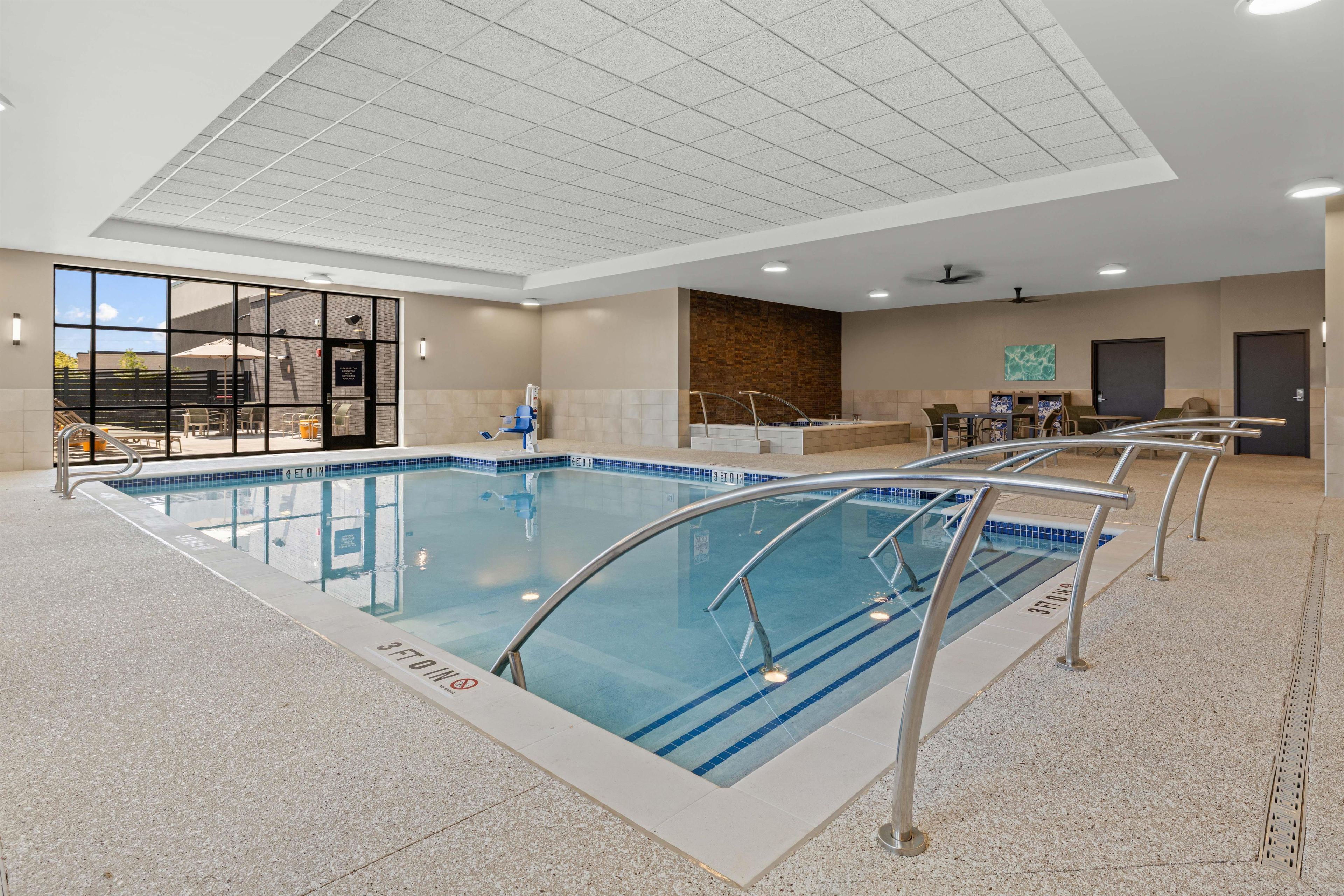 An indoor swimming pool with clear lane markings, a sunroof, and a seating area with tables and chairs.