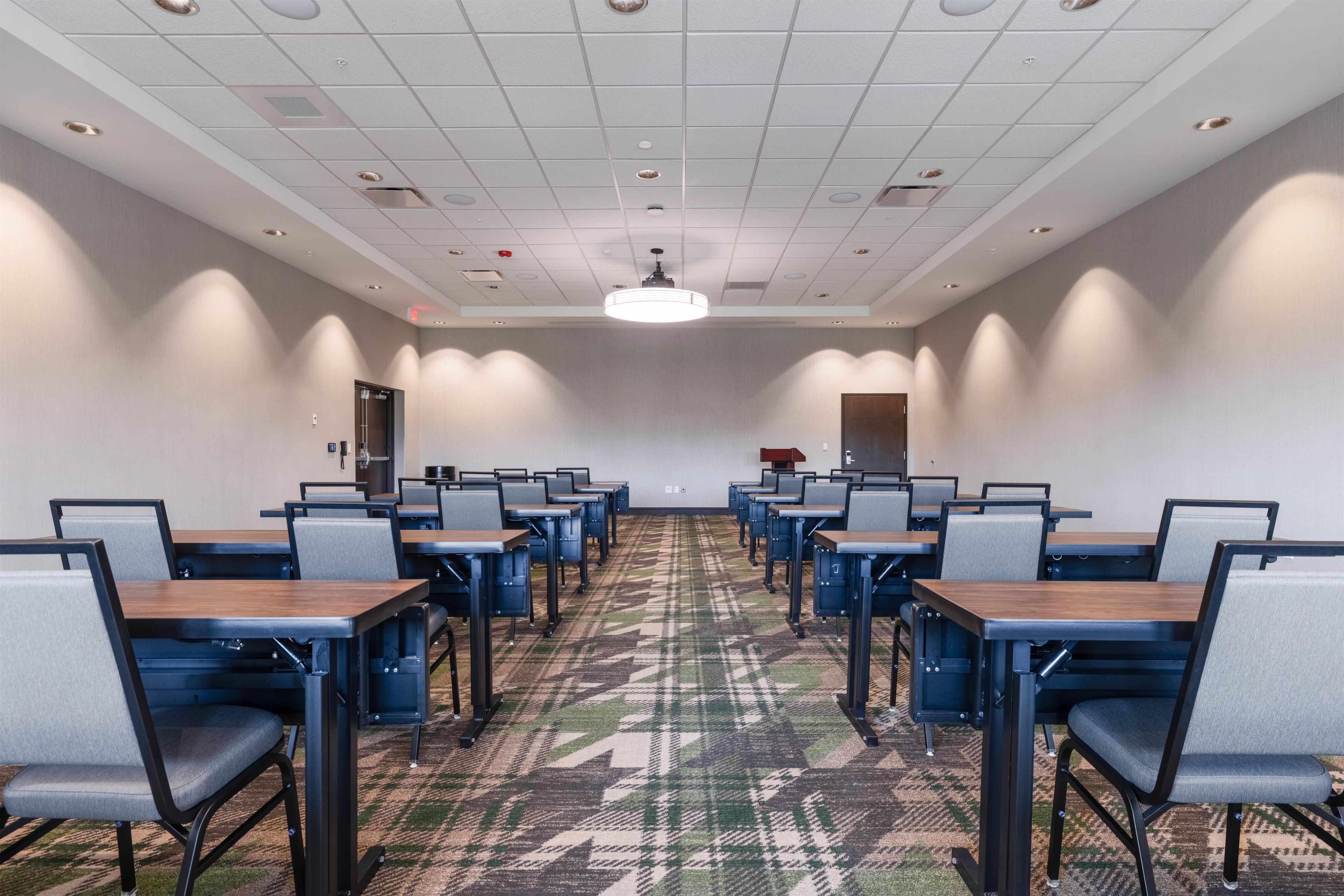 A conference room with rows of tables and chairs, a patterned carpet, and a ceiling with recessed lighting.