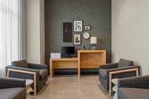 A modern living room with a flat-screen TV, wooden desk, and two armchairs.