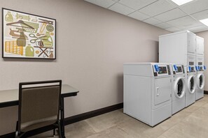 A laundry room with a chair, a table, and stacked washing machines. - Drury Plaza Hotel Nashville Southeast Century Farms (Antioch)