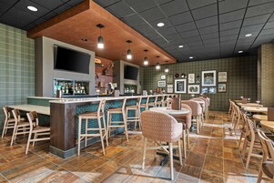 Una zona de bar con barra, taburetes y un área de estar con mesas y sillas.