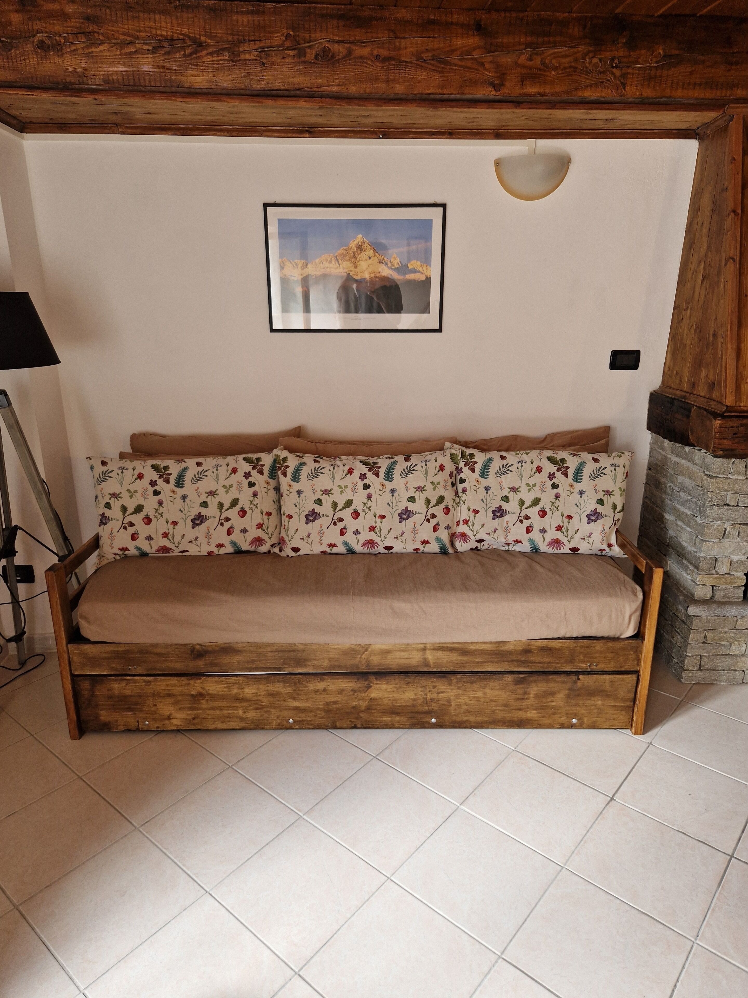 Un canapé en bois avec des coussins à motifs floraux, un tableau encadré accroché au mur et un mur en pierre.