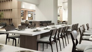 A modern dining area with a long table, multiple chairs, pendant lighting, and a visible kitchen area in the background. - Fairfield Inn & Suites San Luis Potosi Los Lagos (San Luis Potosi)