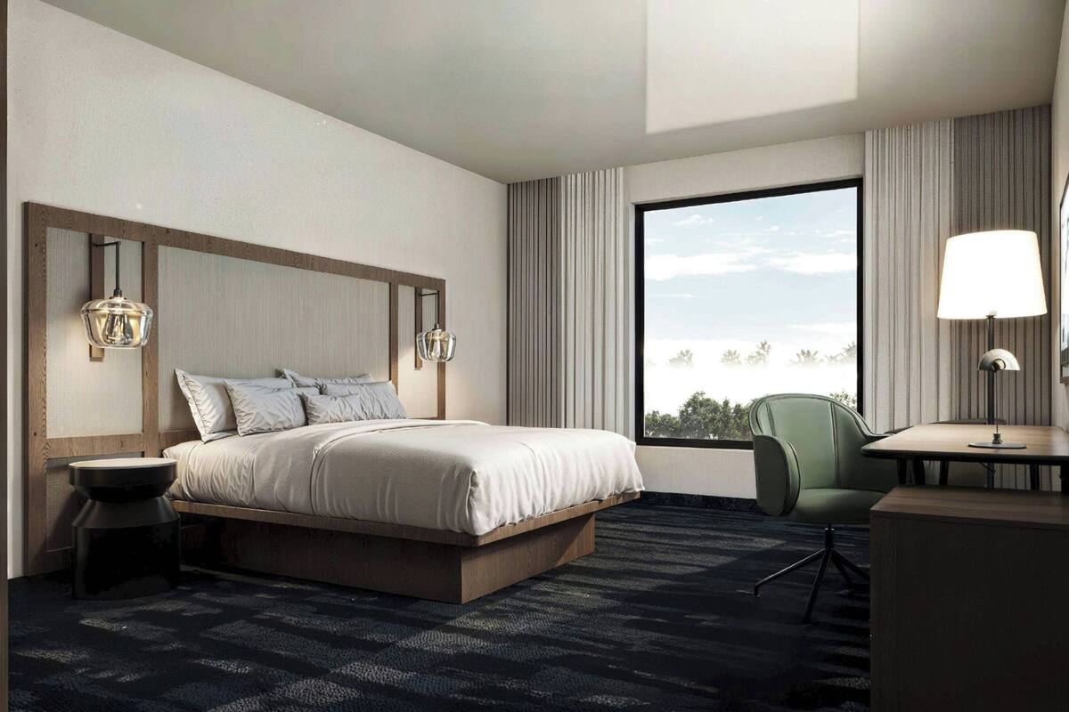 Habitación de hotel moderna con una cama grande, un escritorio, una silla y vistas al exterior.