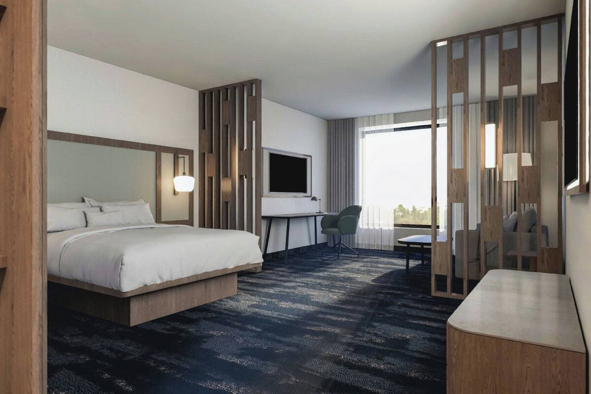 Habitación de hotel con cama, escritorio, silla, televisor y vistas al exterior.