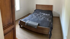 Een slaapkamer met een houten bed, een bedspreide met een wereldkaart print, en een raam dat natuurlijk licht binnenlaat.