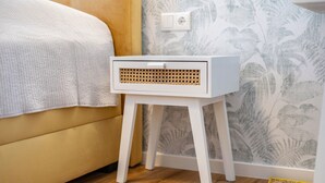 Ett vitt nattduksbord med en flätad frontpanel, en gul soffa och en mönstrad tapet.