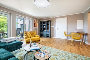 Ein modernes Wohnzimmer mit einer Couch, einem gelben Sessel, einem Essbereich mit Tisch und Stühlen sowie einem Bücherregal.