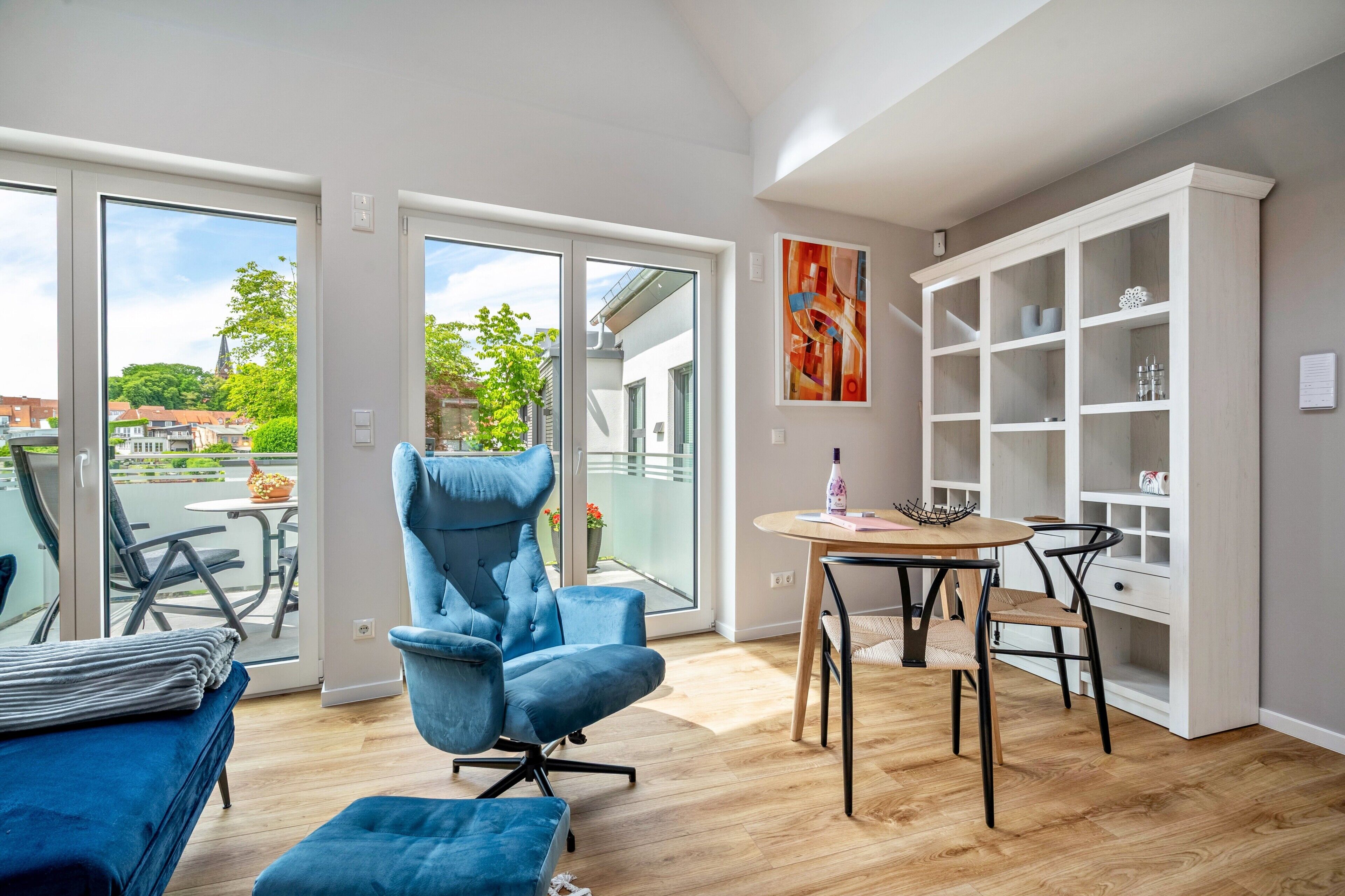 Ein modernes Zimmer mit blauem Sessel, einem Esstisch und einem weißen Schrank.