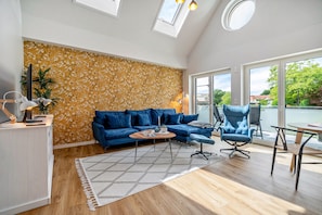 A modern living room with a blue sofa, a round coffee table, and a large window with a view of greenery. - Apartment "Seeblick" with Lake View, Shared Terrace and Wi-Fi (Malchow)