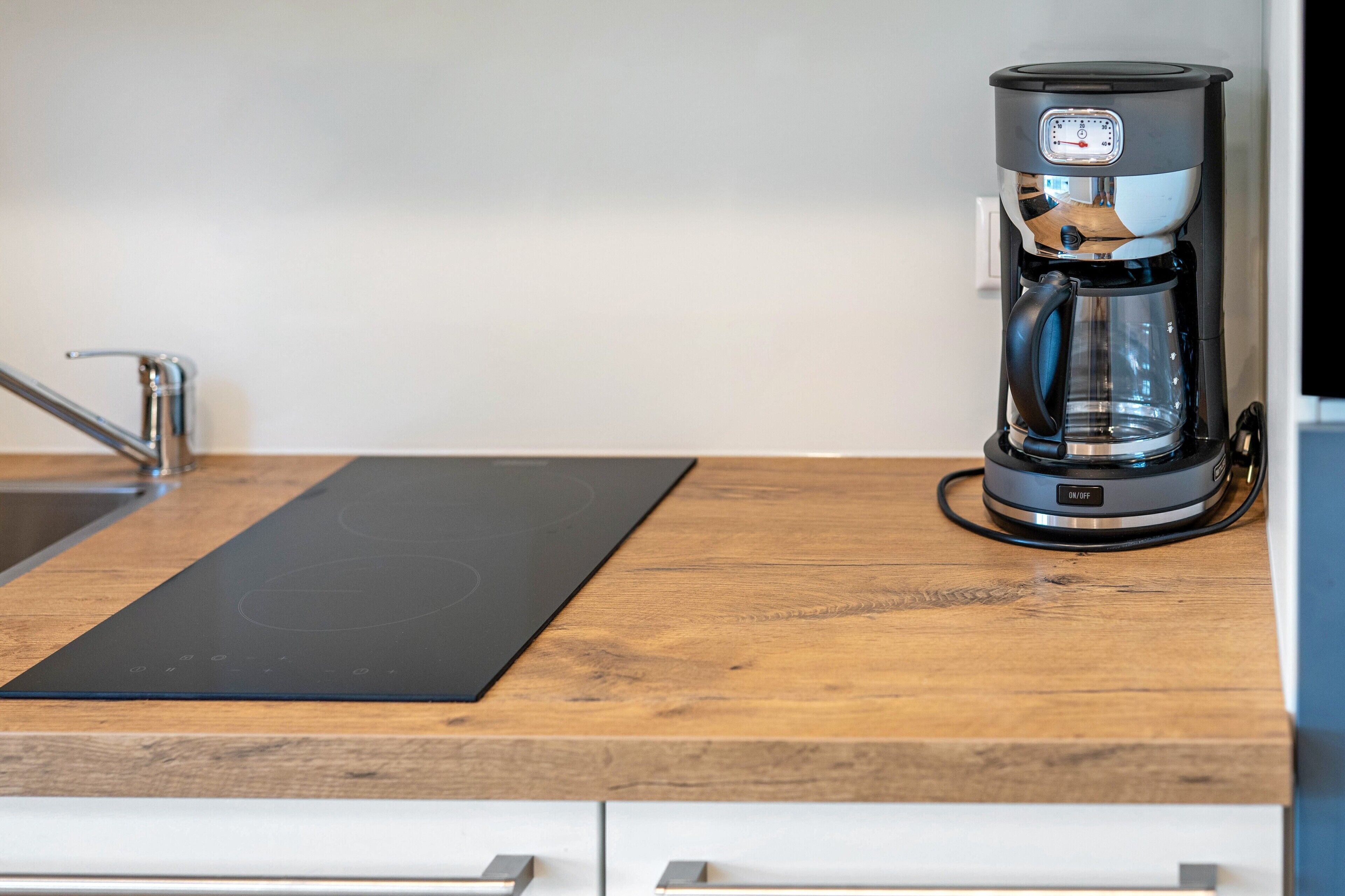A kitchen with a coffee maker on a wooden countertop, a black induction cooktop, and a stainless steel sink.