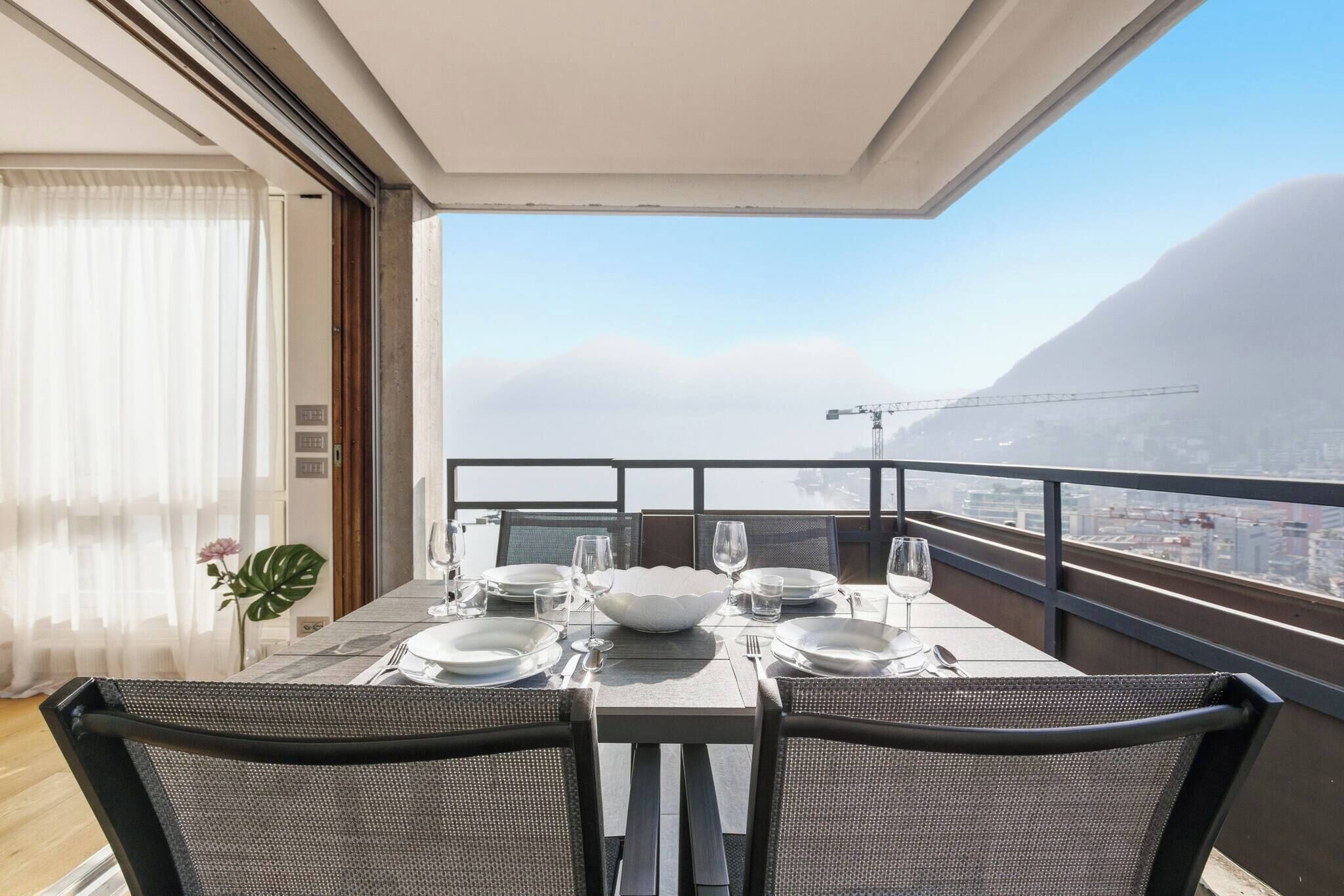 A balcony with a table set for two, overlooking a cityscape and mountains.