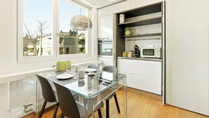 A modern kitchen with a glass dining table, white cabinets, and a view of the outside. - Generoso Luxury Lake View Suite in Lugano (Lugano)