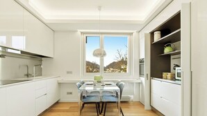 A modern kitchen with a dining table, white cabinets, and a window with a view of the outdoors. - Generoso Luxury Lake View Suite in Lugano (Lugano)