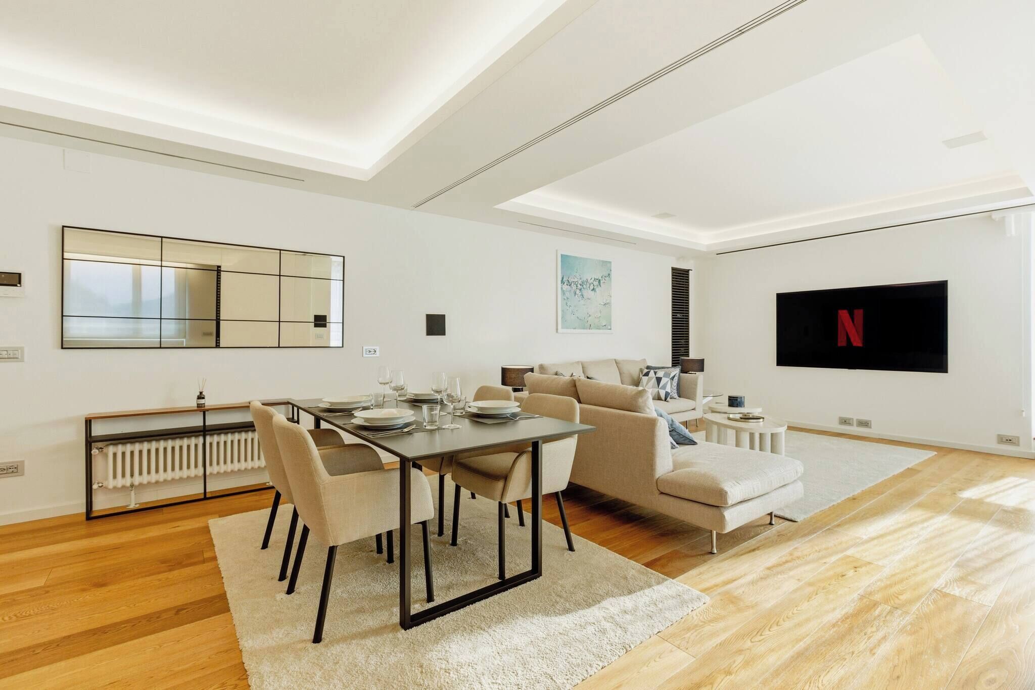 Un salon moderne comprenant un coin repas, un canapé, un téléviseur fixé au mur et un radiateur.