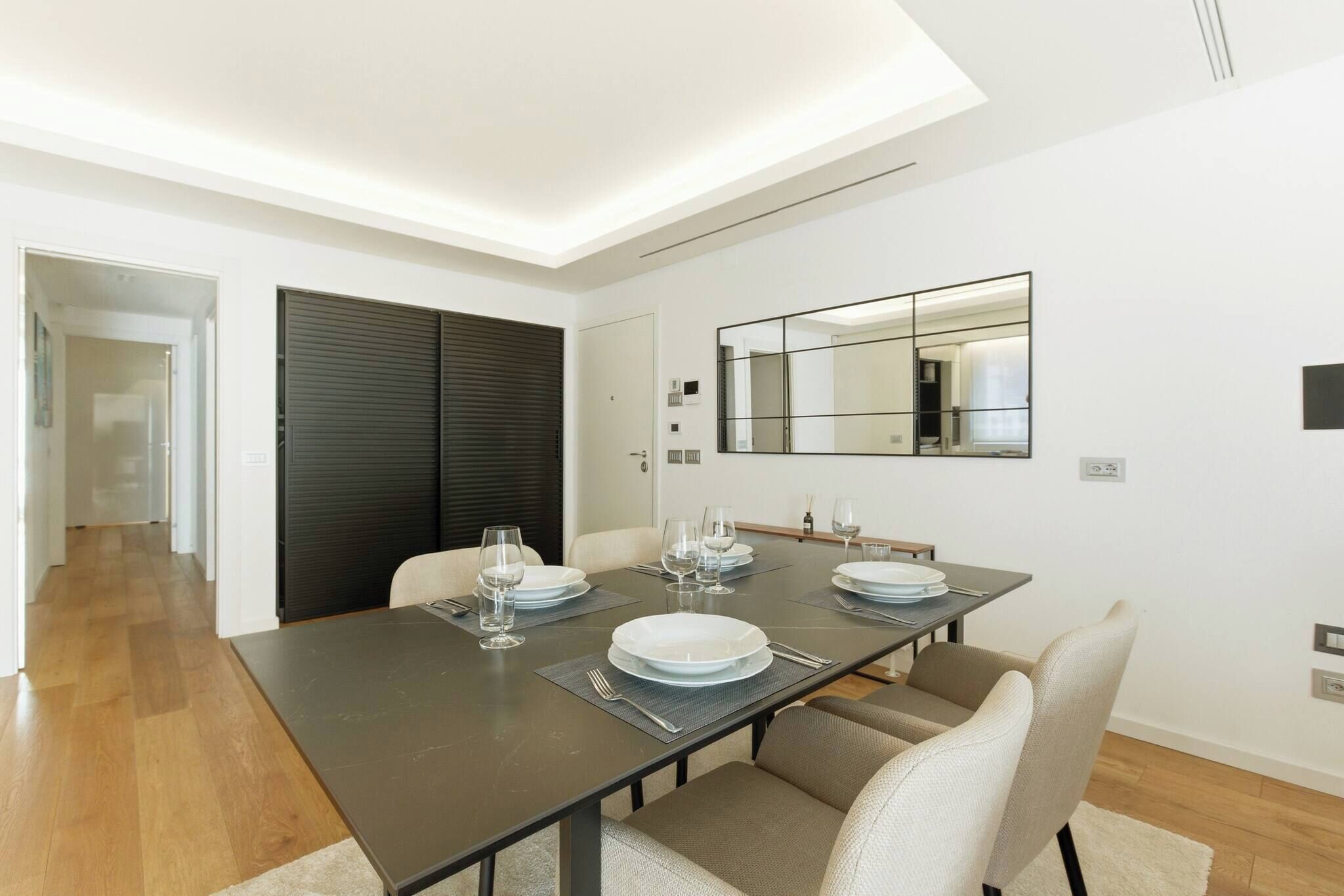 Een moderne eetruimte met een donker houten tafel gedekt voor vier personen, witte borden en glazen.