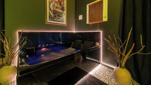 A room with a dark green wall, a blue sofa, a small table, and a decorative plant. - Luxuria Love Room Avignon (Avignon)