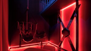 A room with a red-lit ambiance, featuring a hanging chair, a desk, and a chair. - Luxuria Love Room Avignon (Avignon)