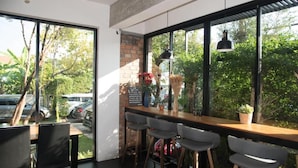 A modern bar area with large windows, bar stools, and hanging pendant lights. - AZZ Hotel (Chiang Mai)