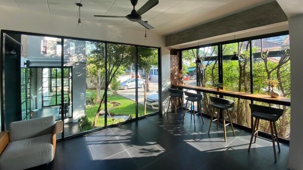 A spacious room with large windows, a ceiling fan, and a seating area with chairs and a table. - AZZ Hotel (Chiang Mai)