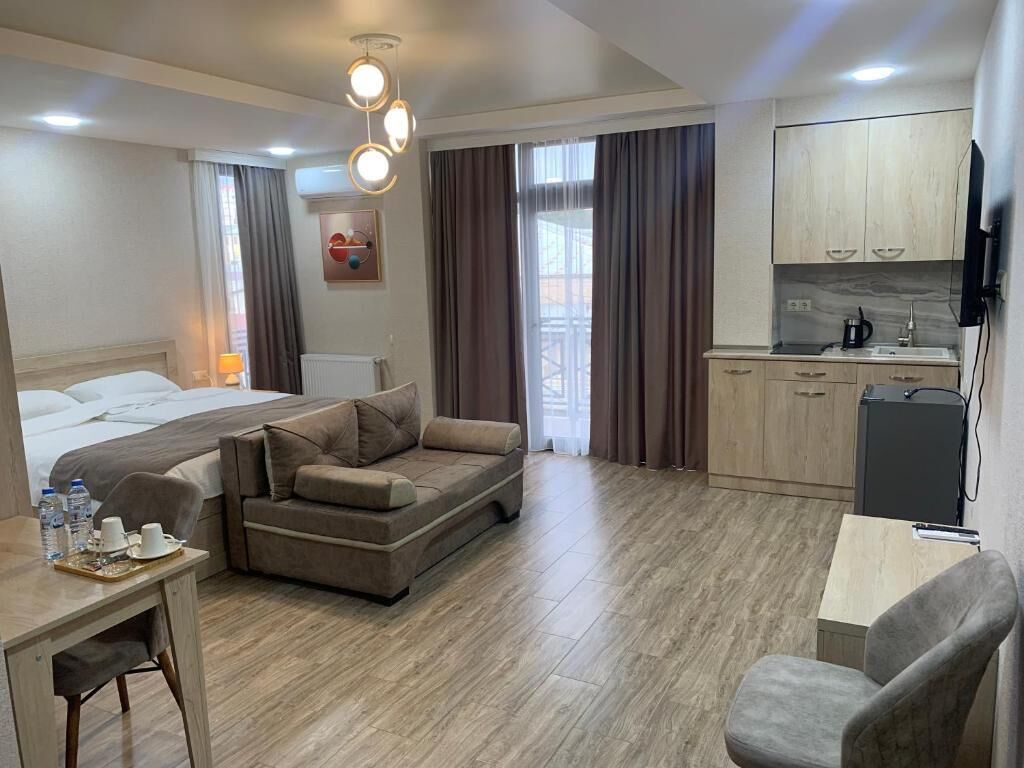 A hotel room with a bed, a sofa, a desk with a chair, a kitchenette, and a TV.