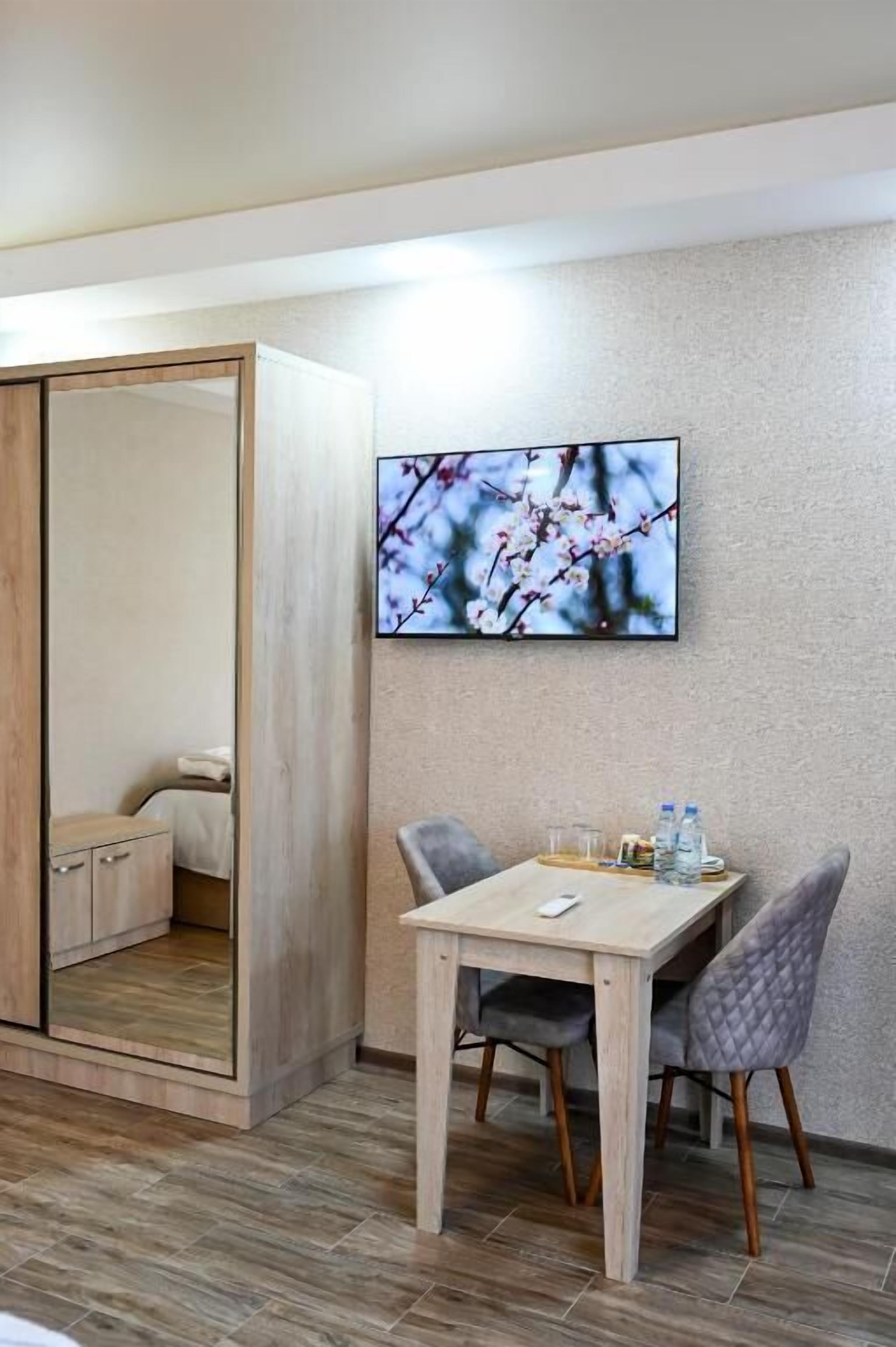 Ein modernes Zimmer mit einem Holzschrank, einem Esstisch mit zwei Stühlen und einem an der Wand befestigten Fernseher, der eine Naturlandschaft zeigt.