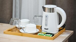 Ein weißes elektrisches Wasserkochteil mit Griff und Bedienfeld auf einer Holzschale.