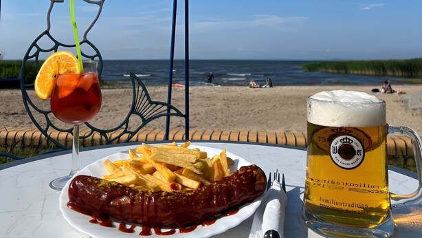 Une table installée sur la plage, avec un repas, une boisson et une sculpture en métal.