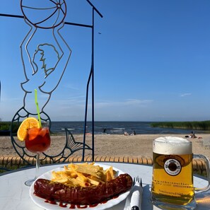 Mesa à beira-mar com refeição, bebida e uma escultura de metal.