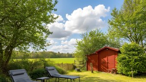 Un abri de jardin rouge, deux fauteuils inclinables et une zone herbeuse avec des arbres et une clôture.
