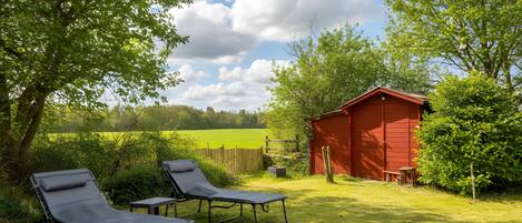 A red shed, two reclining chairs, and a grassy area with trees and a fence.